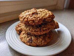 A stack of three freshly baked, chewy oatmeal raisin cookies resting on a white plate.