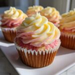 A close-up of a freshly baked strawberry lemonade cupcake topped with a beautiful swirl of yellow and pink frosting.