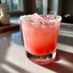 A bright pink, icy Watermelon Margarita served in a rocks glass with a thick salt rim.