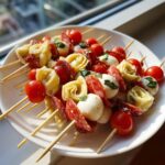 A plate piled high with vibrant Antipasto skewers featuring tortellini, cherry tomatoes, salami, and mozzarella balls.