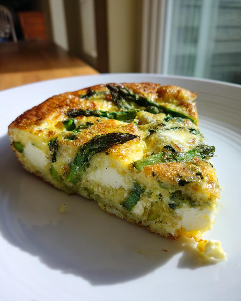 A close-up slice of golden brown Asparagus brie frittata showing chunks of white brie cheese and green asparagus spears.