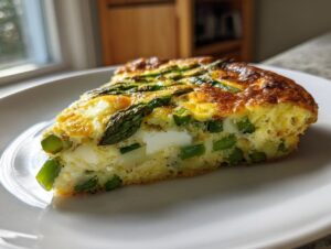 A thick slice of Asparagus brie frittata showing green asparagus pieces and white brie cheese baked into the golden egg base.