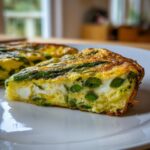 Close-up of a thick slice of Asparagus brie frittata showing green asparagus and white brie cheese pockets in the yellow egg base.