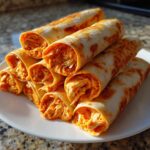 A stack of freshly made Buffalo chicken pinwheels, showing the shredded orange filling inside the lightly browned tortillas.