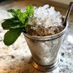 A classic Mint Julep cocktail served in a frosted silver cup, topped high with crushed ice and a fresh mint sprig.