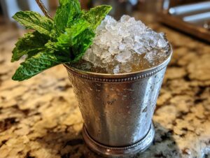 A classic Mint Julep cocktail served in a frosted silver cup, topped with crushed ice and fresh mint.