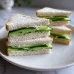 A stack of four triangular Cucumber tea sandwiches made with white bread, cream cheese, and thin cucumber slices.