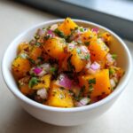 Close-up of vibrant, chunky homemade mango salsa featuring diced orange mango, red onion, and cilantro in a small white bowl.