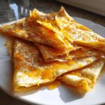 Close-up of folded Crepes Suzette on a white plate, glistening with rich orange caramel sauce.