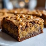 A close-up, tempting shot of a thick square of butterscotch brownies topped with melted butterscotch chips.