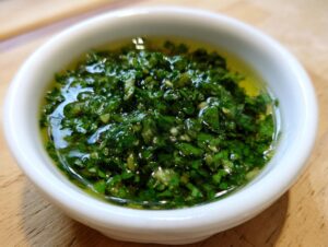Close-up of vibrant green, chunky homemade mint sauce swimming in liquid, served in a small white ramekin.