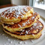 A close-up of a stack of three fluffy Lemon Ricotta Pancakes dusted heavily with powdered sugar.