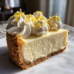 A close-up slice of No bake lemon cheesecake featuring a thick graham cracker crust and topped with whipped cream and lemon zest.