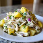 A close-up of a serving of Pineapple Avocado Chicken Salad featuring shredded chicken, chunks of pineapple, and red onion.