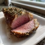 Close-up of a medium-rare roast leg of lamb slice, crusted with herbs.