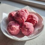 Five bright pink, slightly textured strawberry yogurt bites served in a small white bowl lined with parchment paper.