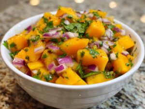 Close-up of bright orange Mango salsa featuring diced mango, red onion, and cilantro in a white bowl.